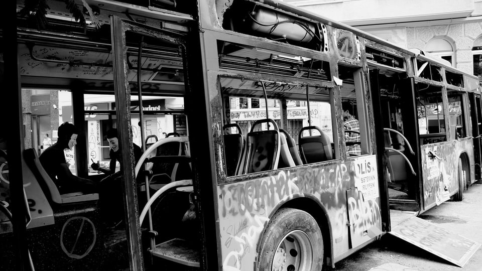 Zwei Männer mit Maske sitzen in einem leeren Bus.