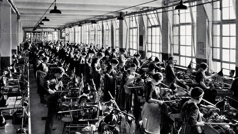 Ein Schwarz-Weiss-Bild: Viele Frauen und Männer arbeiten in einer Revolver-Dreherei.