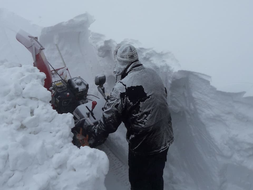 Eine Person versucht mit einem Schneeräumgerät die Massen wegzuschleudern.