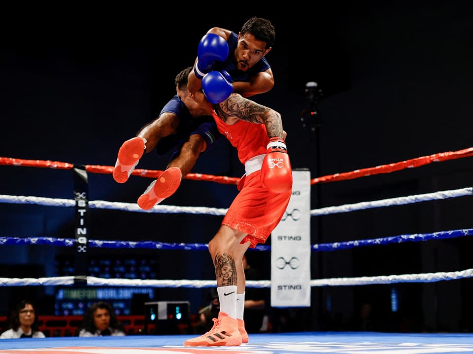Zwei Boxer im Ring während eines Kampfes, einer in roter Ausrüstung hebt den anderen in blauer Ausrüstung hoch.