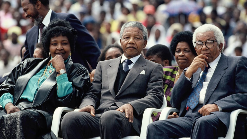 Menschenmenge sitzt wartend auf einer Tribüne. Vorne mittig ist Nelson Mandela zu erkennen.