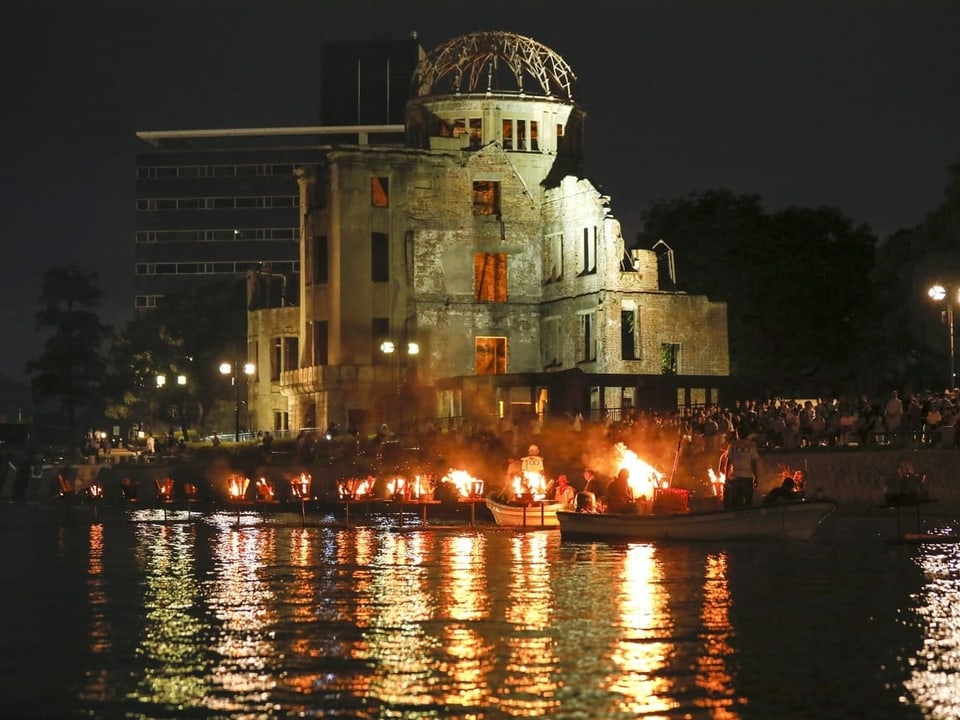 Blick auf das ehemalige Regierungsgebäude und Menschen, die mit Feuern in Schiffen den Opfern des Atombombenangriffs gedenken.