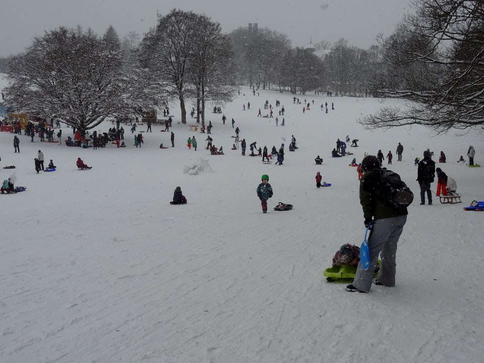 Kinder und Erwachsen tummeln sich auf der Schlittenwiese am Gurten, es schneit leicht.