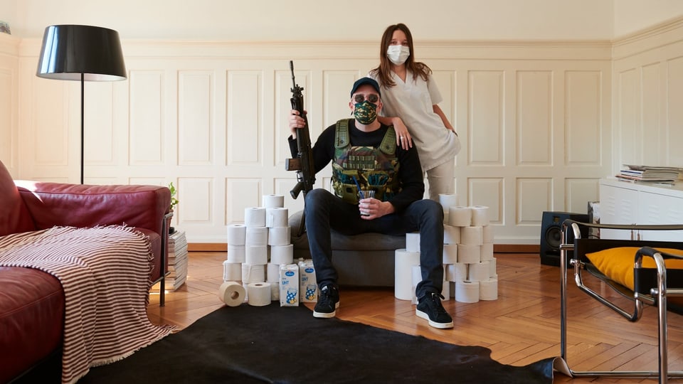 Eine Krankenschwester und ein Mann mit Maske und Sturmgewehr, umgeben von WC-Papier.