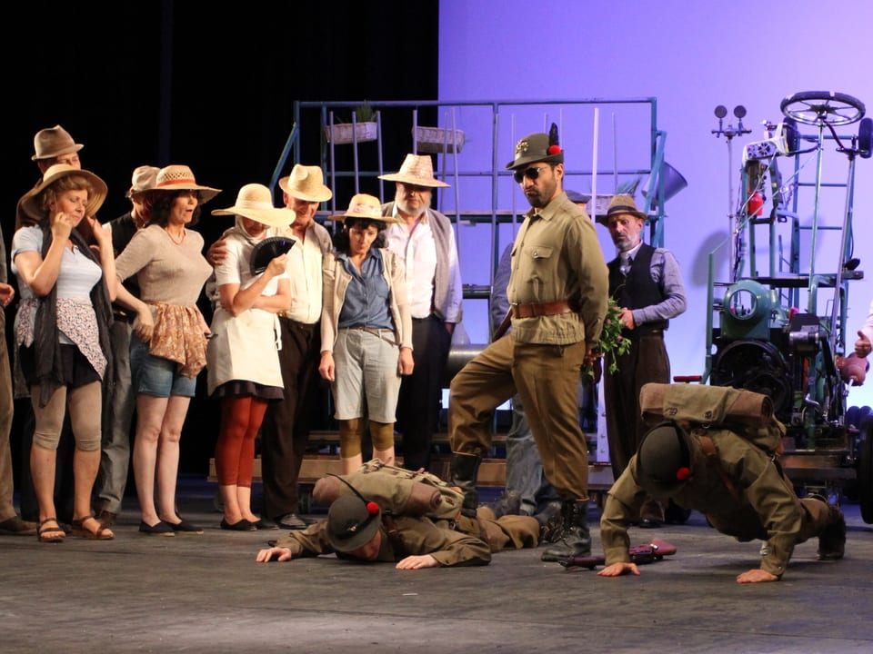 Darsteller Belcore trägt zusammen mit zwei weiteren Personen Soldatenuniform, mehrere Damen schauen der Szenerie zu.