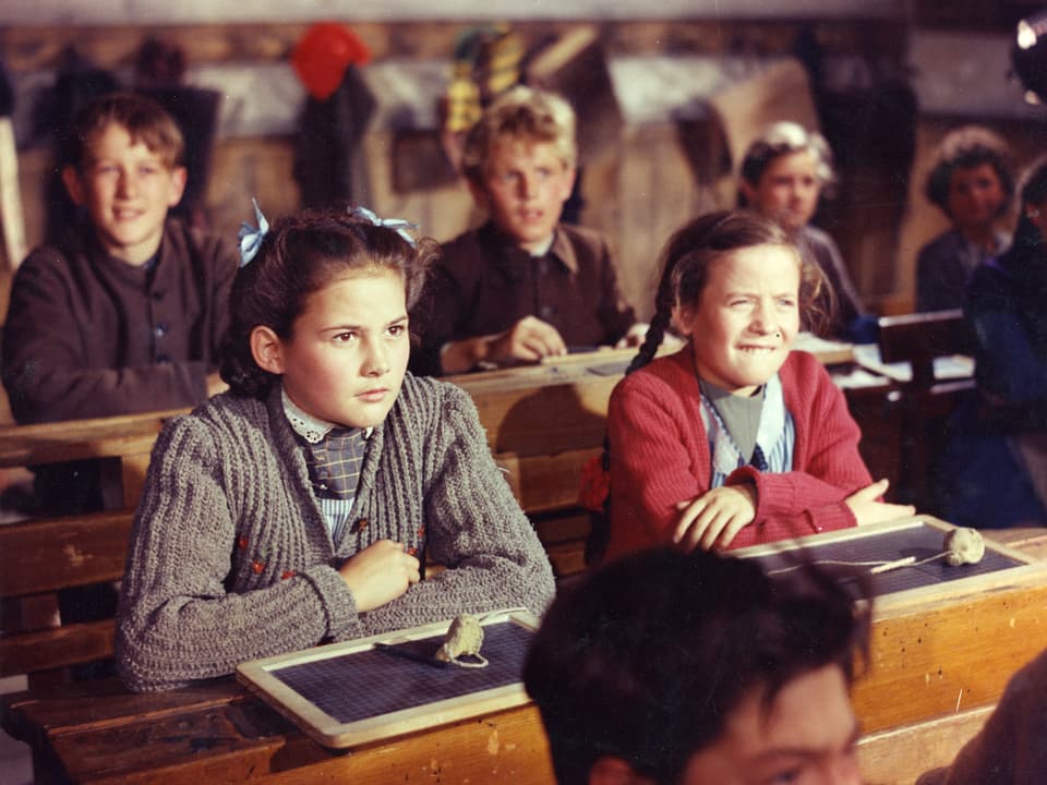 Heidi sitzt in der Schulbank. Andere Kinder sitzen neben und hinter ihr.