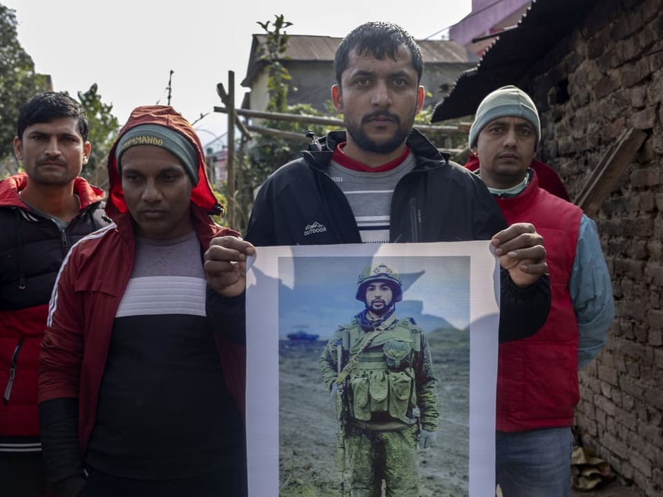 Vier Männer stehen nebeneinander mit traurigem Blick. Einer hält ein Bild eines Soldaten.