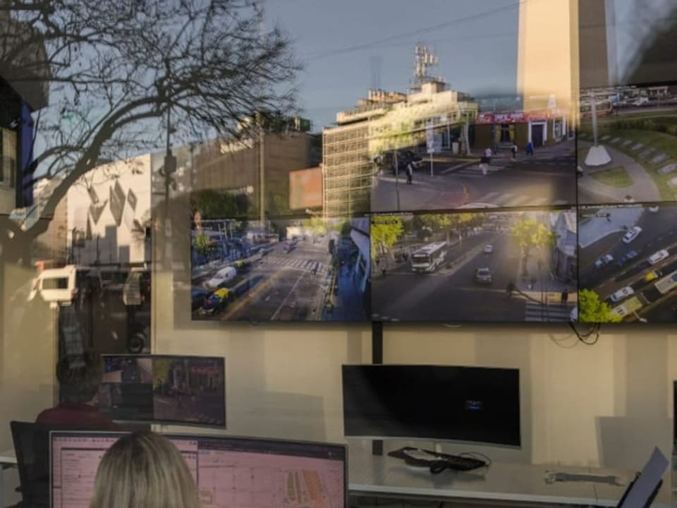 Eine Frau vor einem Computer, entfernt auf der Wand ein Grossbildschirm mit Bildern vom Stadtzentrum beim Obelisken.