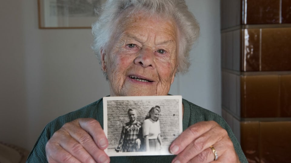 Ältere Frau hält lächelnd ein Schwarz-Weiss-Foto in der Hand