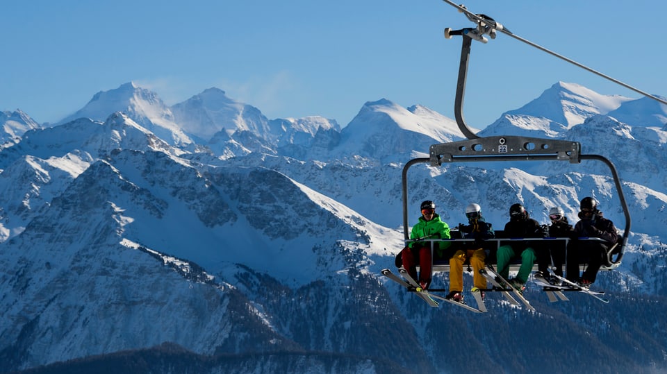 Skifahrer auf einem Sessellift, im Hintergrund verschneite Berghänge.