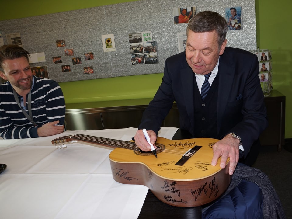 Der Sänger steht an einem Tisch und schreibt auf eine Gitarre.
