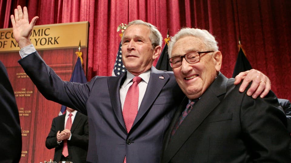 Bush links streckt Hand Haus und hält Kissinger. Er lacht in Kamera.