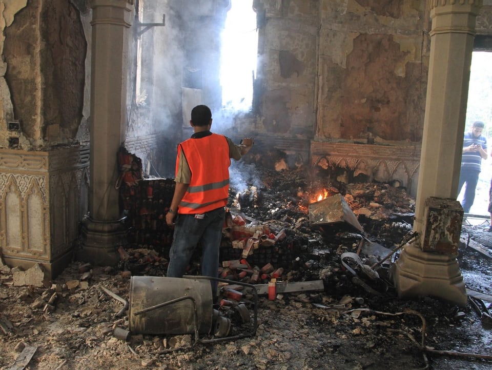 In der schwer beschädigten Moschee liegen Schutt und Asche am Boden, ein Mann betrachtet die Schäden.
