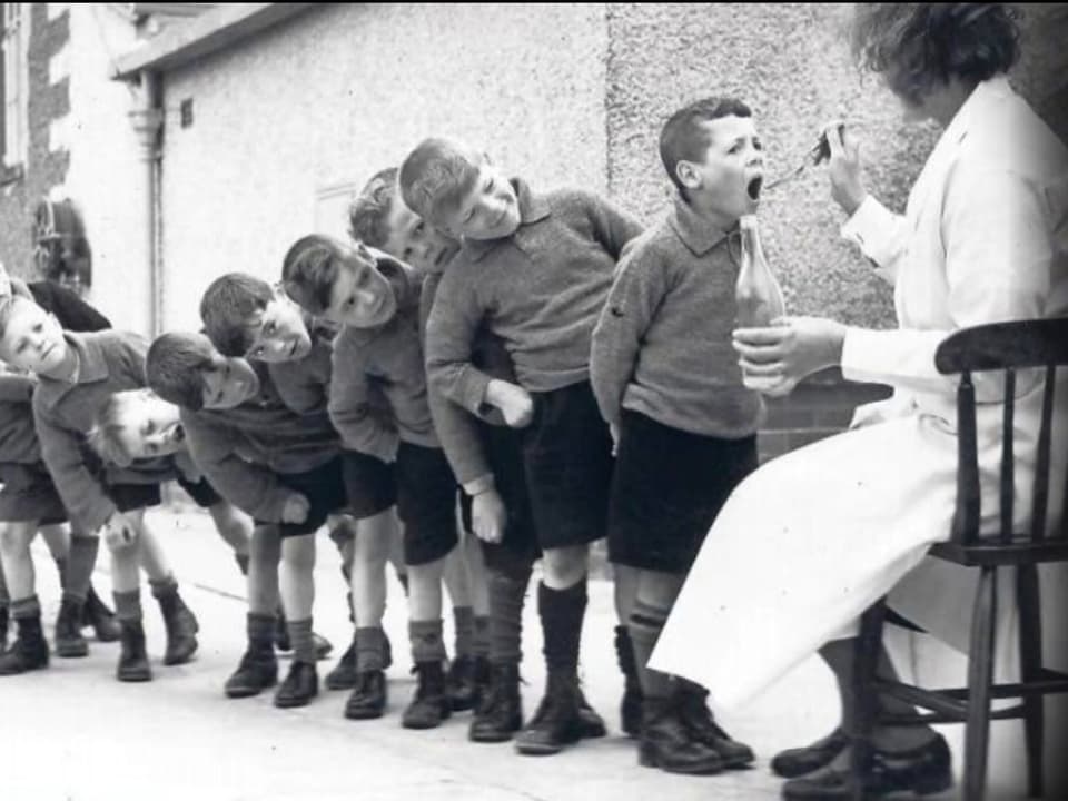 Kinder stehen an, um einen Löffel Lebertran zu bekommen.