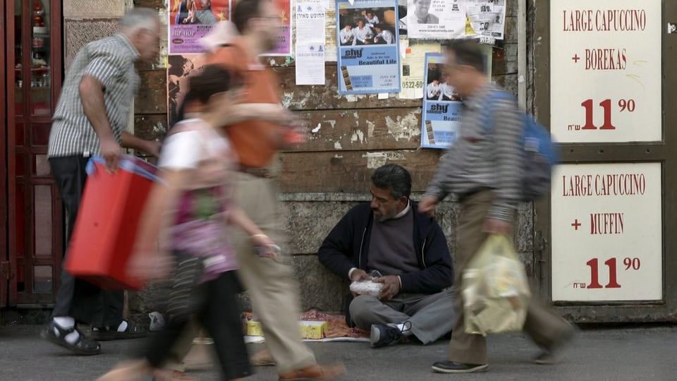 Menschen auf der Jaffastrasse gehen durchs Bild (verwischt), ein Bettler sitzt am Boden.