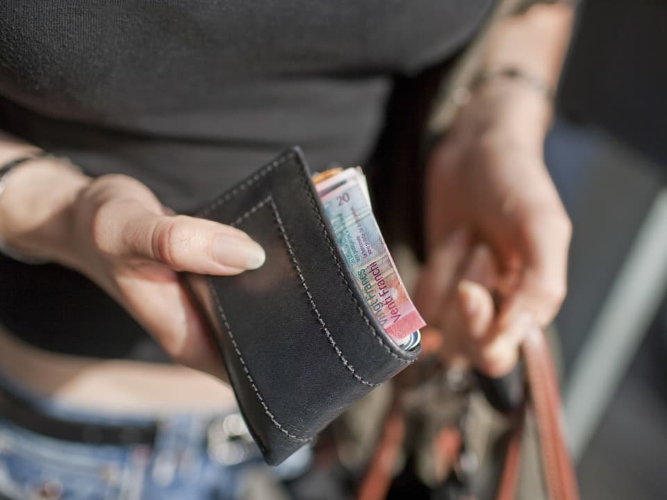 Eine Frau hält ein Portemonnaie in der Hand. Der Rand einer 20-Franken-Note ist zu sehen.