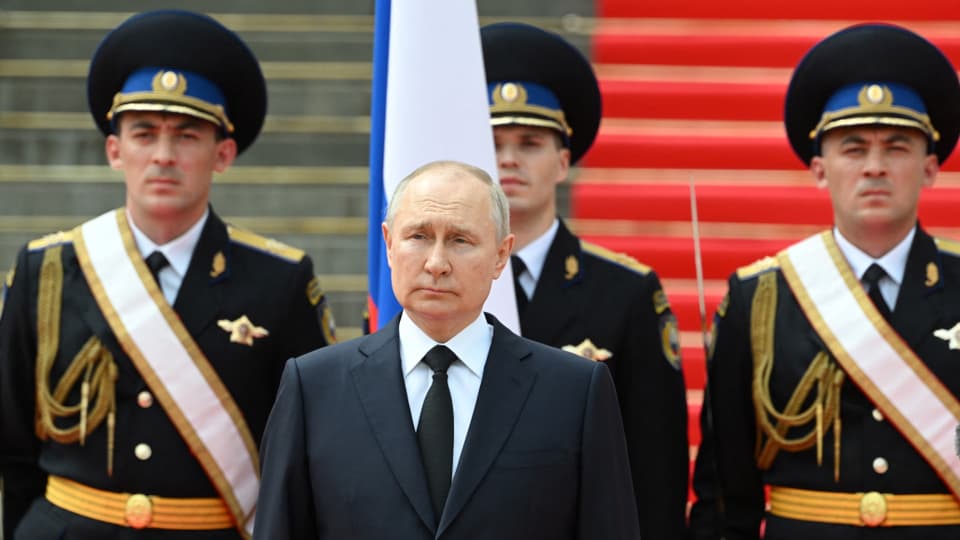 Wladimir Putin an einer Militärparade; hinter ihm stehen drei Soldaten in Uniform