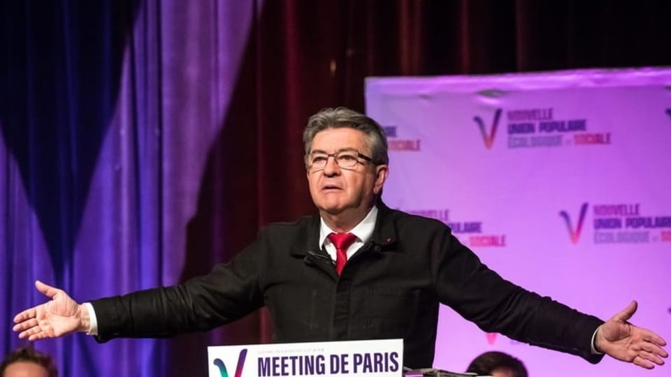 Jean-Luc Mélenchon gestikulierend vor einem Podium und Publikum an einem Wahlkampfanlass