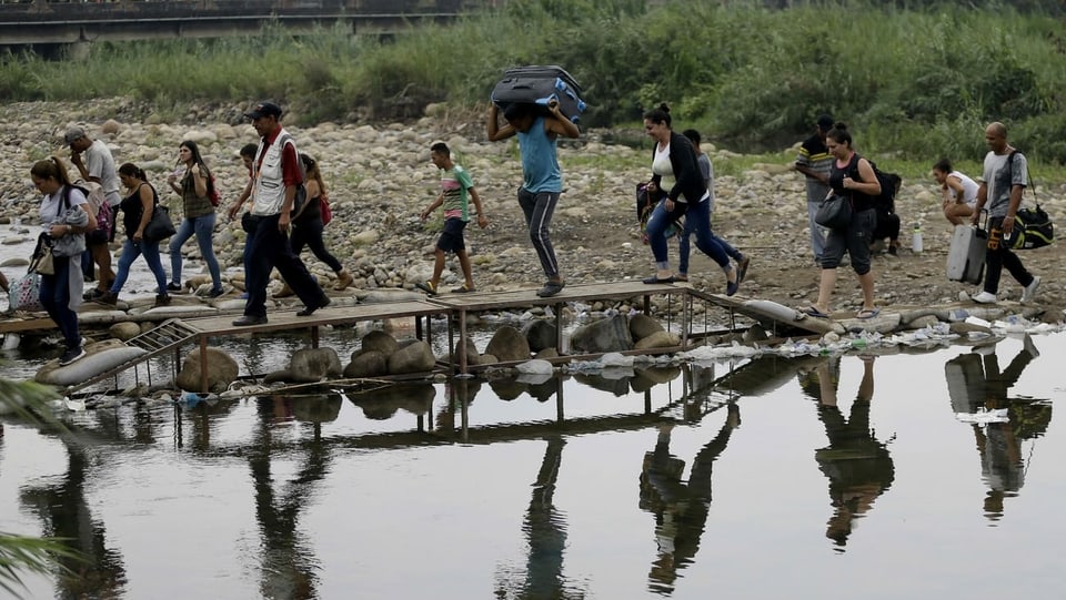 Eine Gruppe Flüchtlinge überquert mitsamt Koffern und Taschen via Holzsteg einen Fluss.