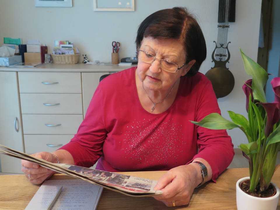 Eine Frau sitzt an einem Tisch und liest Zeitung