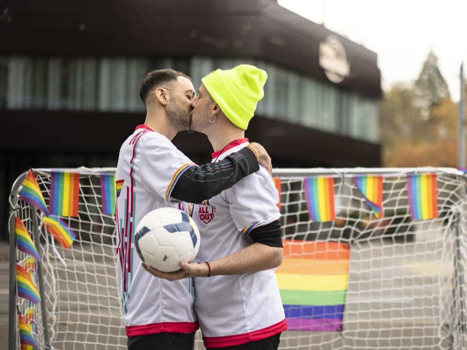Zwei Personen küssen sich beim Protest vor dem Fifa-Museum in Zürich. Es hat mehrere Regenbogenfahnen.