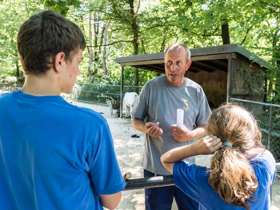 Zooangestellter und zwei Kinder, der Mann weist die Kinder an, was zu tun ist.