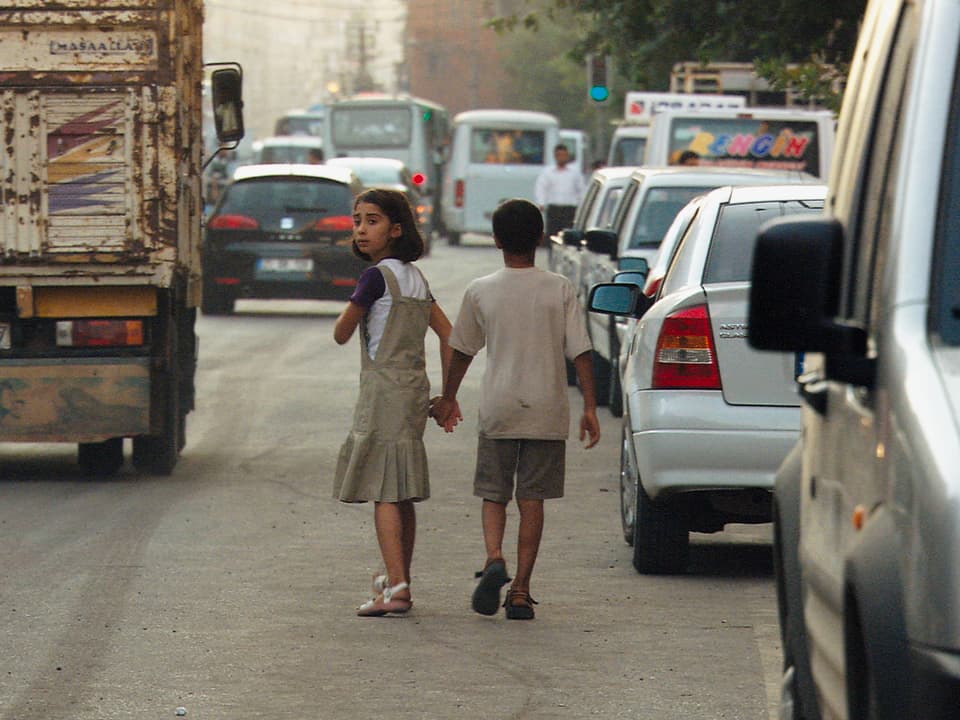 Zwei kleine Kinder spazieren Hand in Hand auf der Strasse zwischen Autos.