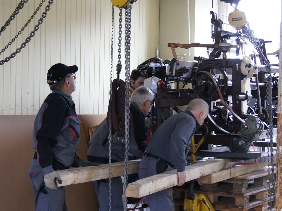 Der über 100-jährige Webstuhl wird im Inneren der Fabrik mit Hilfe von Kanthölzern auf ein Palett geschoben.