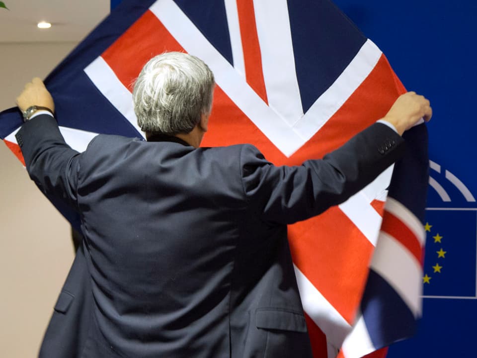 Eine Person hängt eine britische Fahne vor das EU-Logo des EU-Parlamentes.