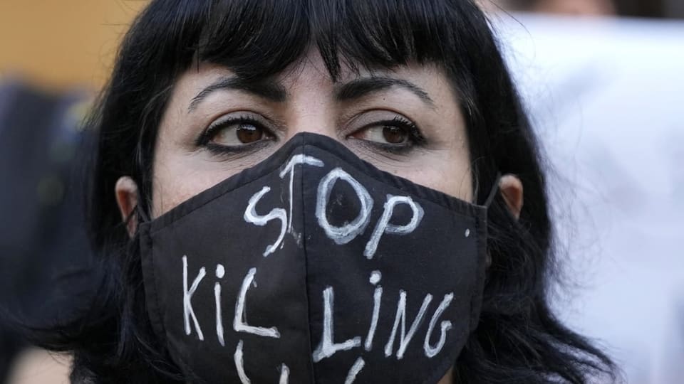 Eine junge Frau mit einem Mundschutz, auf dem steht: Hört auf, uns zu töten