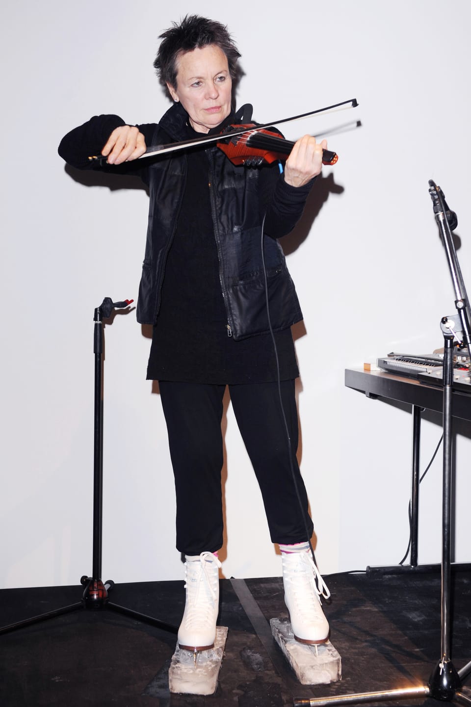 Laurie Anderson spielt Geige und trägt dabei Schlittschuhe mit Eisblöcken an den Kufen.