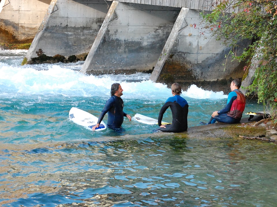 Drei Surfer im Wasser vor einer Fluss-Schleuse