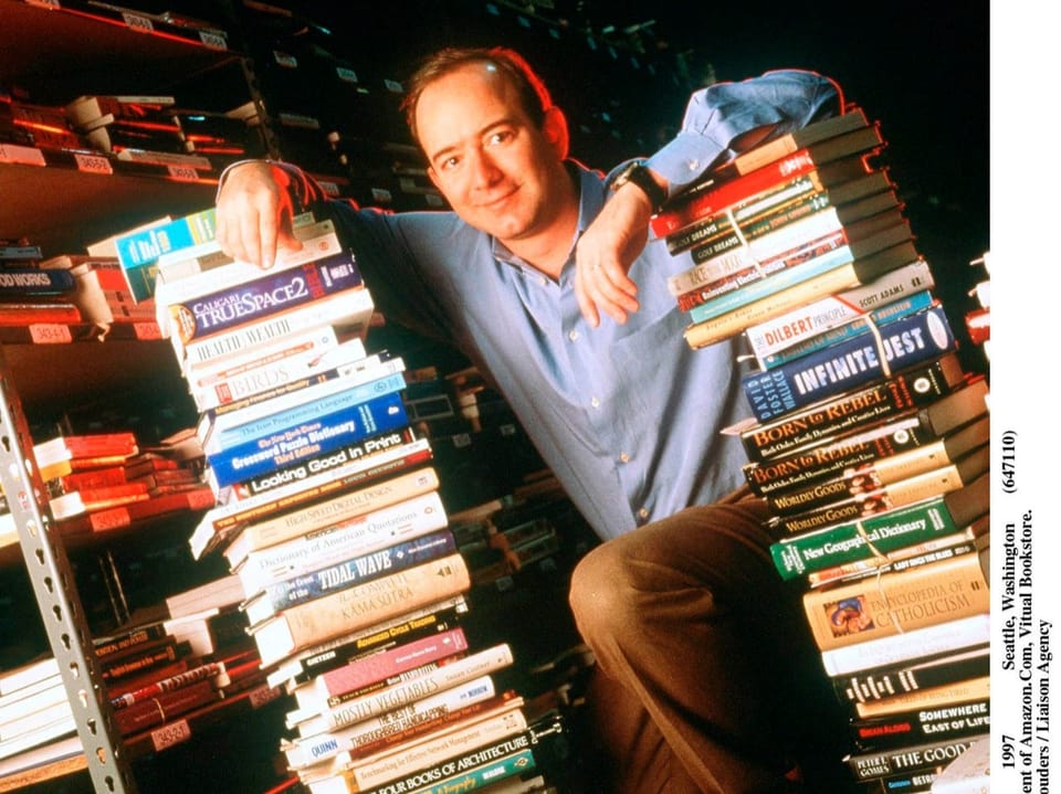 Jeff Bezos als junger Mann zwischen Bücherstapeln. 