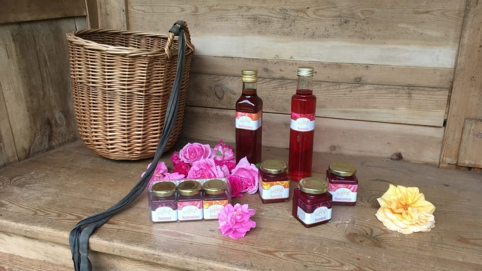 Rosenblüten und Produkte aus Rosenblättern stehen auf einem Holztisch.