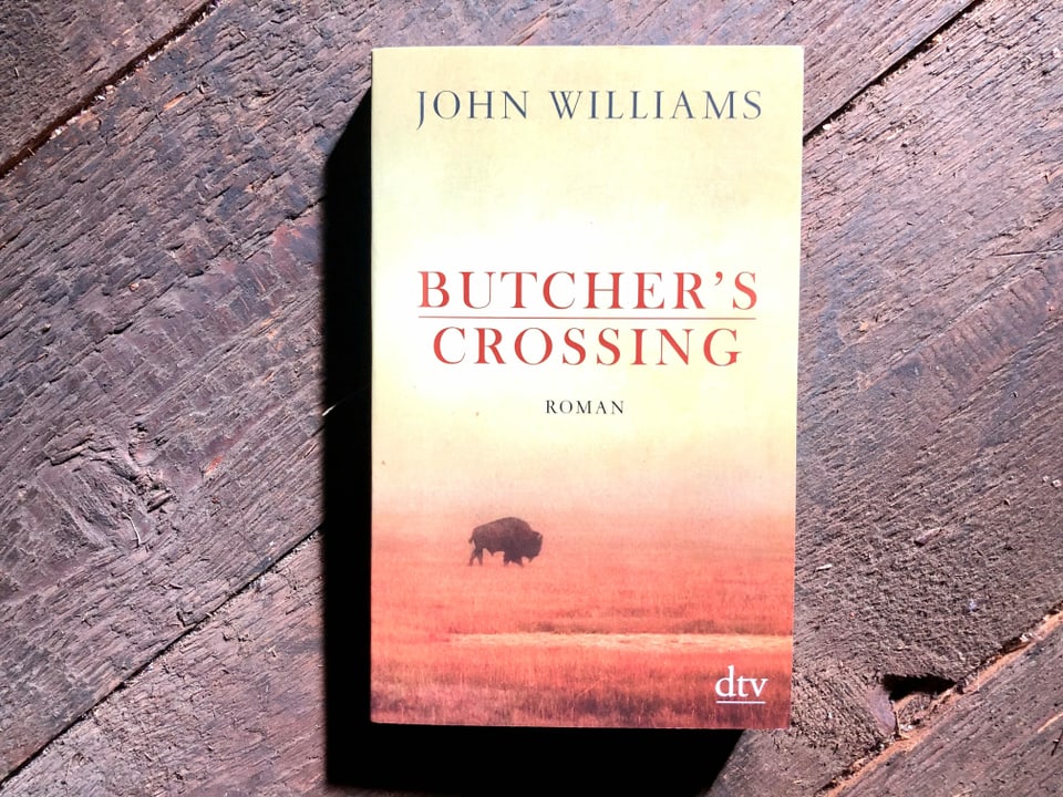Western Nummer 2 «Butcher’s Crossing» von John Williams liegt auf einem dunklen Dielenboden