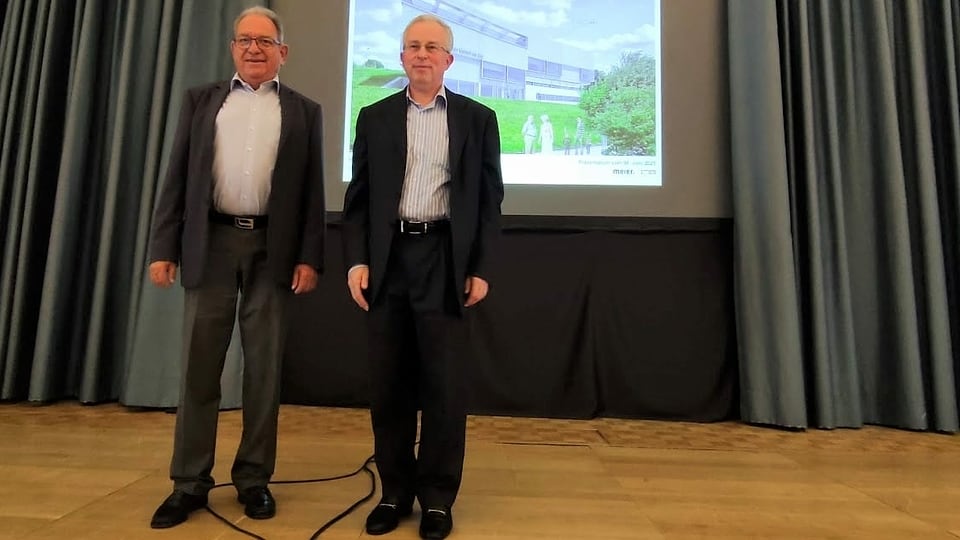 Zwei Männer im Anzug vor einer Leinwand.