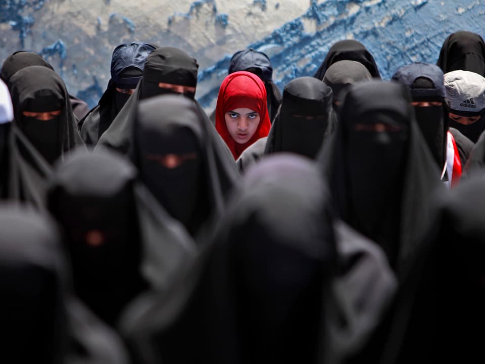 Verschleierte Frauen, in der Mitte ein Mädchen mit rotem Kopftuch. 