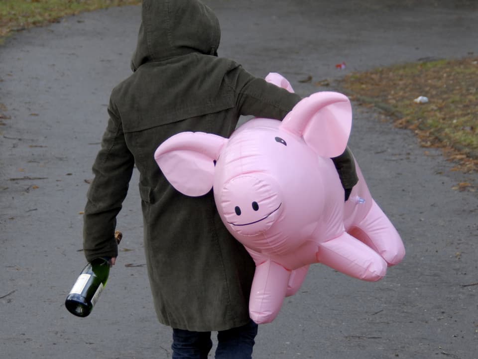 Person trägt Sektflasche und aufblasbares Plastikschwein 
