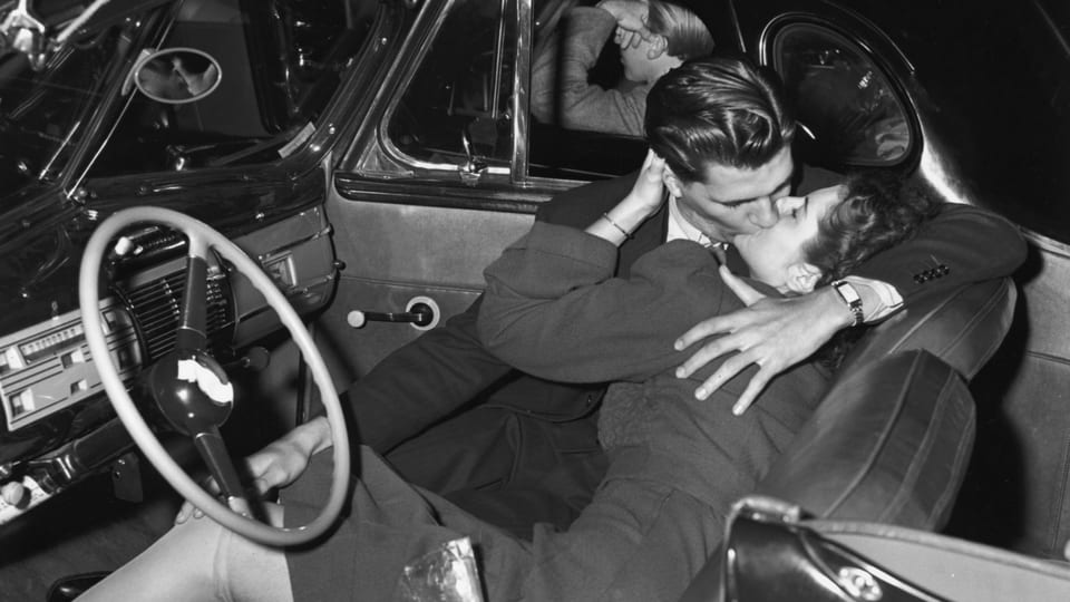 Ein altes schwarz-weiss-Foto: Eine Frau und ein Mann küssen sich in einem Auto.