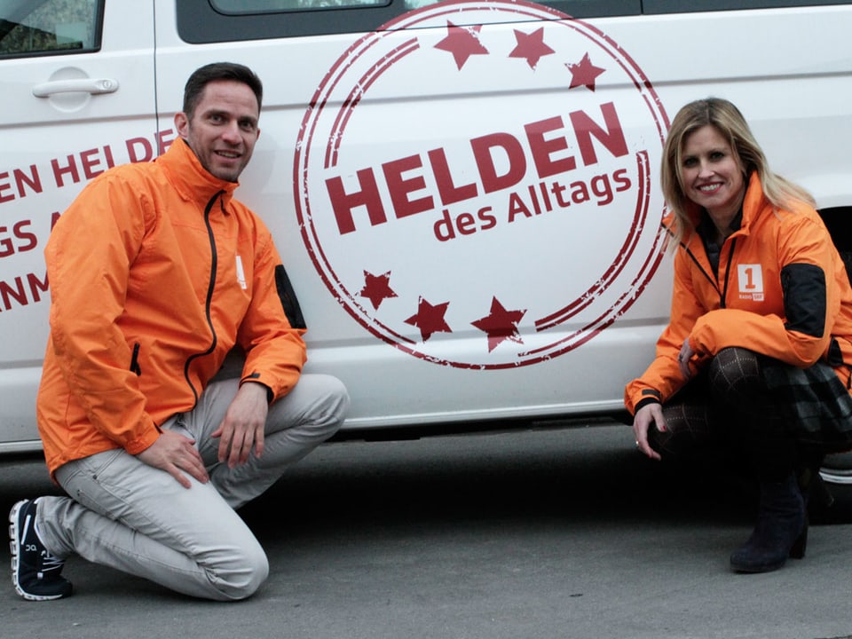 Adrian Küpfer und Sabine Dahinden knien vor dem Auto, auf dem Helden des Alltags steht.
