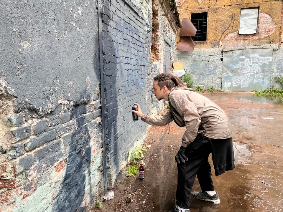 Ein Künstler der Künstlergruppe «YAV» sprüht Schatten von Menschen auf eine Mauer in einem Innenhof.