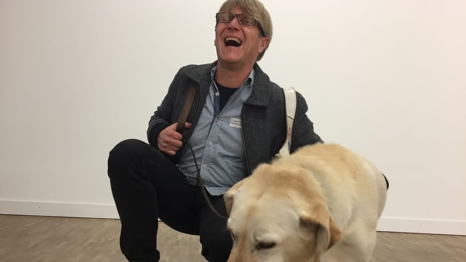 Alexander Wyssmann mit seinem Blindenführhund sitzt und lacht. 