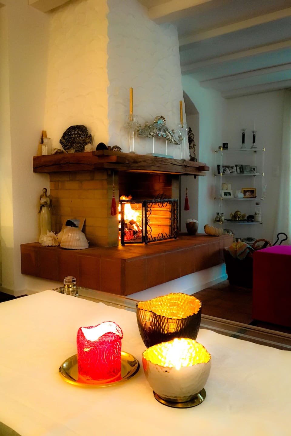Tisch mit drei Kerzen, im Hintergrund ein brennendes Cheminée.