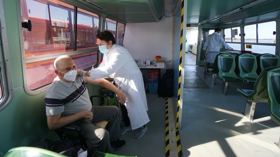Ein älterer Mann im T-Shirt bekommt von einem Arzt im weissen Kittel auf einem Boot die Corona-Impfung.