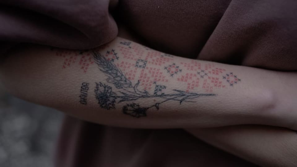 Frau zeigt Tattoos auf Unterarm: traditionelles Ornament, eine Ähre und das Wort «Jugend».