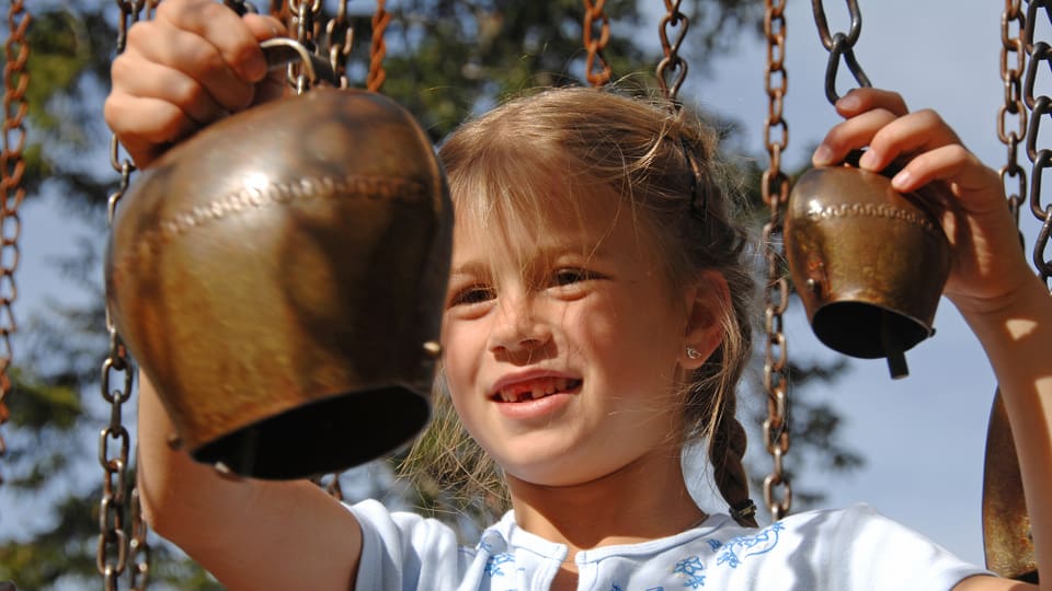 Ein kleines Mädchen bringt zwei kleine Glocken zum Klingen.