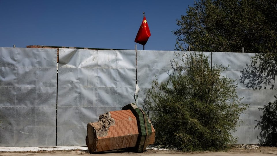 ein zerstörtes Minarett, hinter einer Absperrung weht die chinesische Flagge.