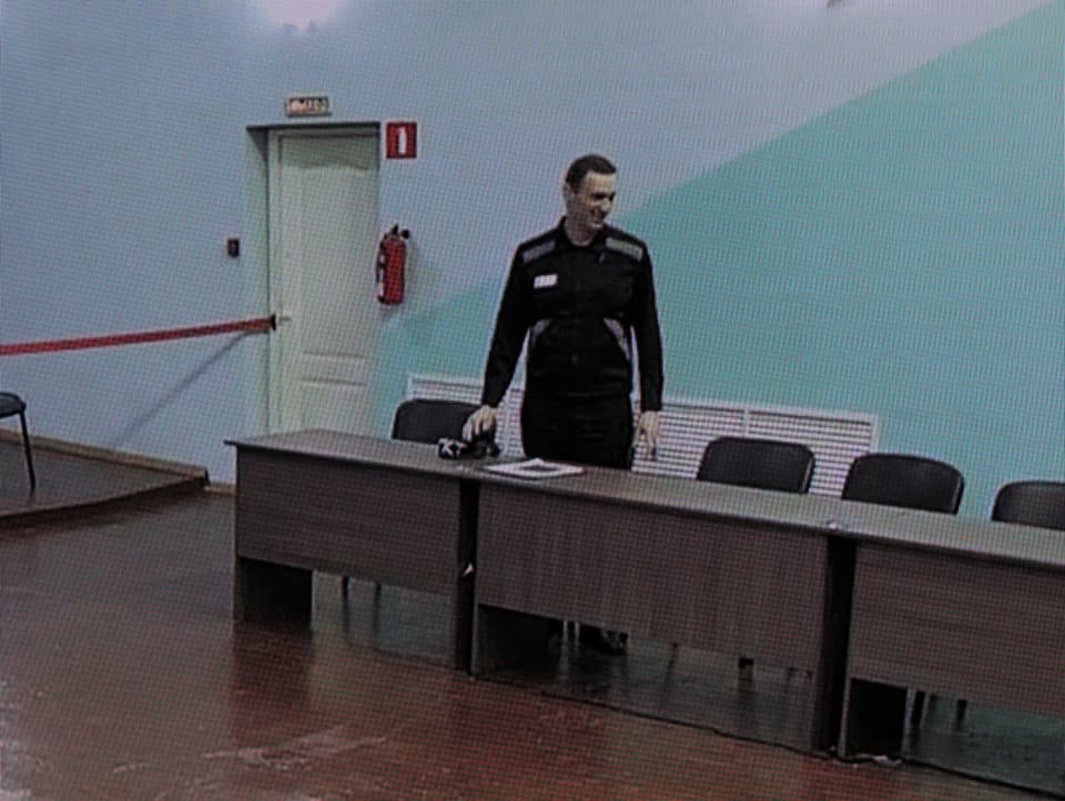 Eine Fotografie eines Bildschirms, auf dem Alexej Nawalnys zu sehen ist. Er steht an einer Reihe von Tischen.