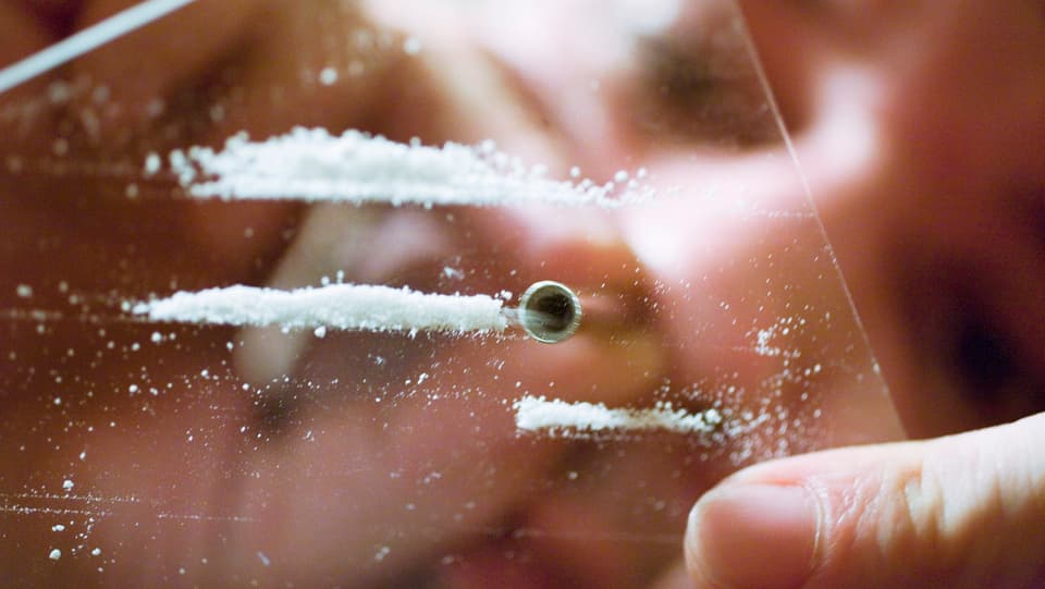 Person von unten fotografiert schnupft Kokain ab einer Glasplatte.