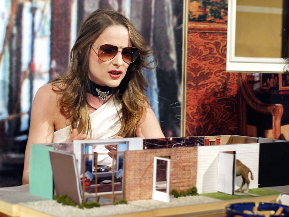Eine Frau mit Sonnenbrille vor einem Modell eines Hauses.